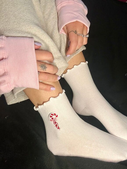 Chaussettes blanches courtes avec petits froufrous à l’extrémité, 100% coton. Personnalisation des chaussettes grâce à des broderies. Il faut choisir parmi un choix de broderies dessinées à la main sur le thème de l’hiver, Noël, fêtes fin d’année, winter. La broderie est présente sur le côté extérieur des chaussettes. Toutes les broderies sont faites à la commande selon la personnalisation choisie. Ici, il s’agit de la broderie sucre d'orge porté
