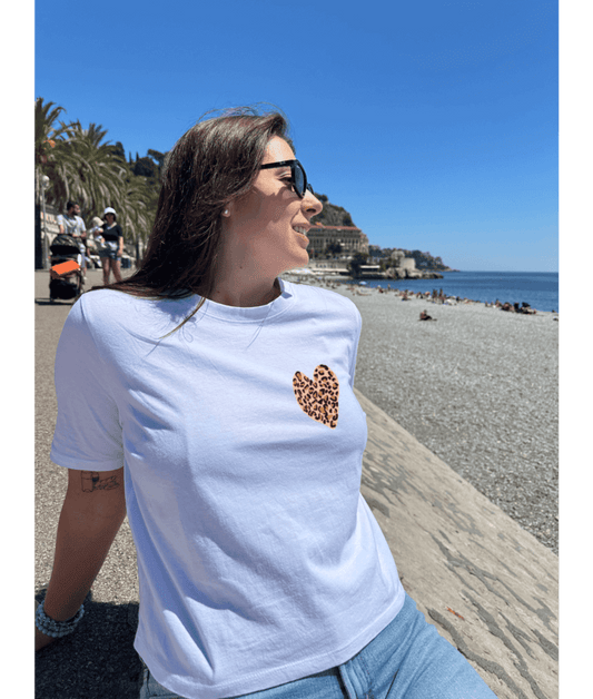 T-shirt oversize blanc, manche courte, 100% coton. Personnalisation du t-shirt grâce à une technique de flocage, le DTF, pour une meilleure qualité d’impression et de tenue. La personnalisation est floquée à l’avant au milieu en haut et à l’arrière en grand dans le dos. Ici, il s’agit de la personnalisation de DTF coeur léopard. Plage promenade des Anglais, Nice 06 été soleil.