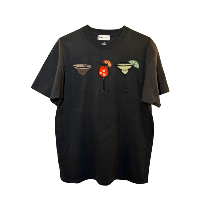 T-shirt oversize noir, 100% coton. Personnalisation du t-shirt grâce à des broderies. Il faut choisir parmi un choix de broderies dessinées à la main sur le thème de l’été sur la Côte d’Azur dans les Alpes Maritimes, 06. Il faut aussi choisir la position de la broderie entre à gauche côté cœur, à droite ou au milieu. Toutes les broderies sont faites à la commande selon la personnalisation choisie. Ici, il s’agit de la broderie 3 cocktails : espresso martini, Aperol spritz et margarita.
