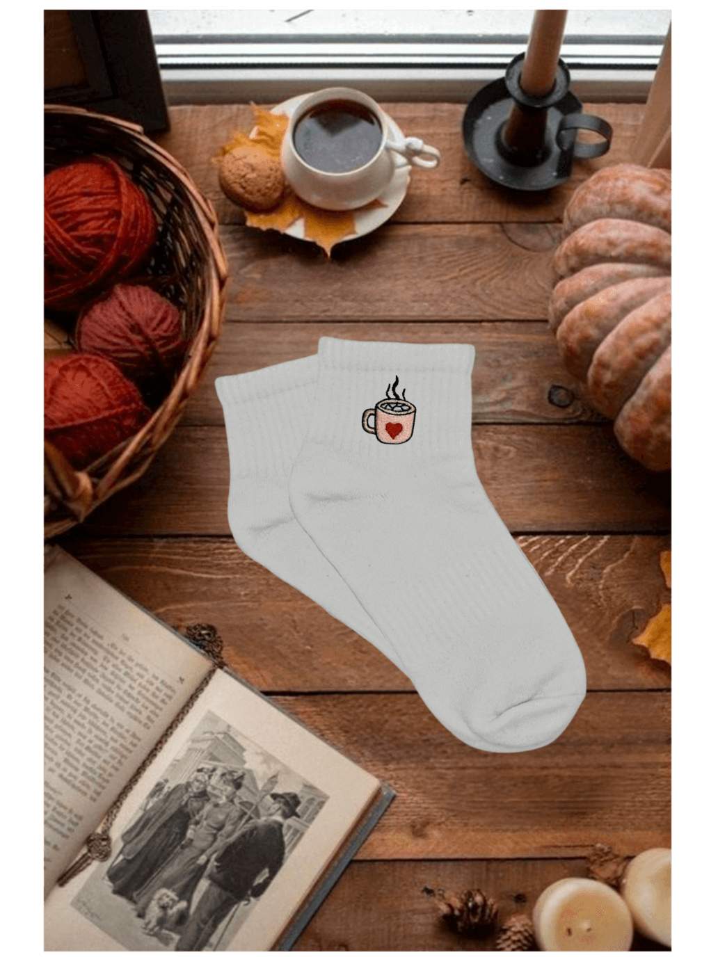 Paire de chaussettes basses blanches en coton. Broderie sur le côté tasse de chocolat chaud rose avec un coeur rouge et des marshmallows. Dans un décor automnal, cozy, citrouille, bougie, livre, pelotte de laine, café. Idée personnalisation broderie automne.