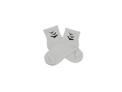 Chaussettes blanches courtes, 100% coton. Personnalisation des chaussettes grâce à des broderies. Il faut choisir parmi un choix de broderies dessinées à la main sur le thème de l’automne, saison automnale, Halloween, broderie cosy. La broderie est présente sur le côté extérieur des chaussettes. Toutes les broderies sont faites à la commande selon la personnalisation choisie. Ici, il s’agit de la broderie chauve-souris, noir.