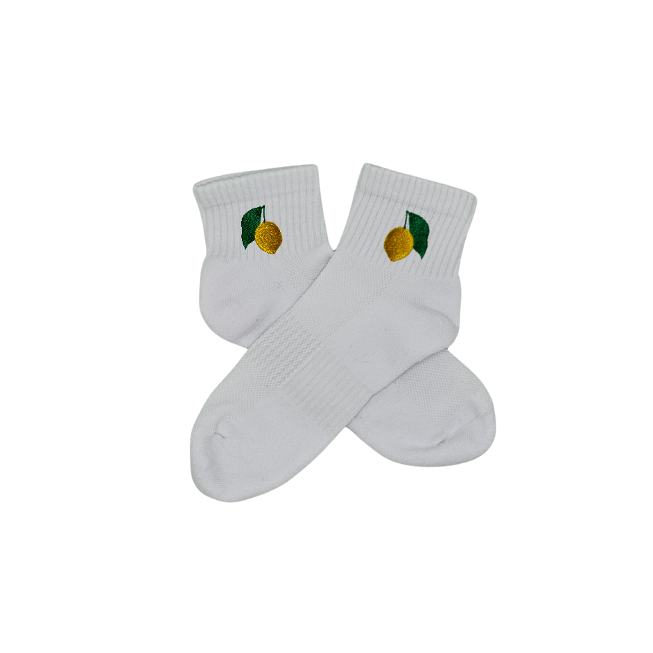 Chaussettes blanches courtes, 100% coton. Personnalisation des chaussettes grâce à des broderies. Il faut choisir parmi un choix de broderies dessinées à la main sur le thème de l’été sur la Côte d’Azur dans les Alpes Maritimes, 06. La broderie est présente sur le côté extérieur des chaussettes. Toutes les broderies sont faites à la commande selon la personnalisation choisie. Ici, il s’agit de la broderie citron de Menton, jaune et vert. Emblème de la ville de Menton.