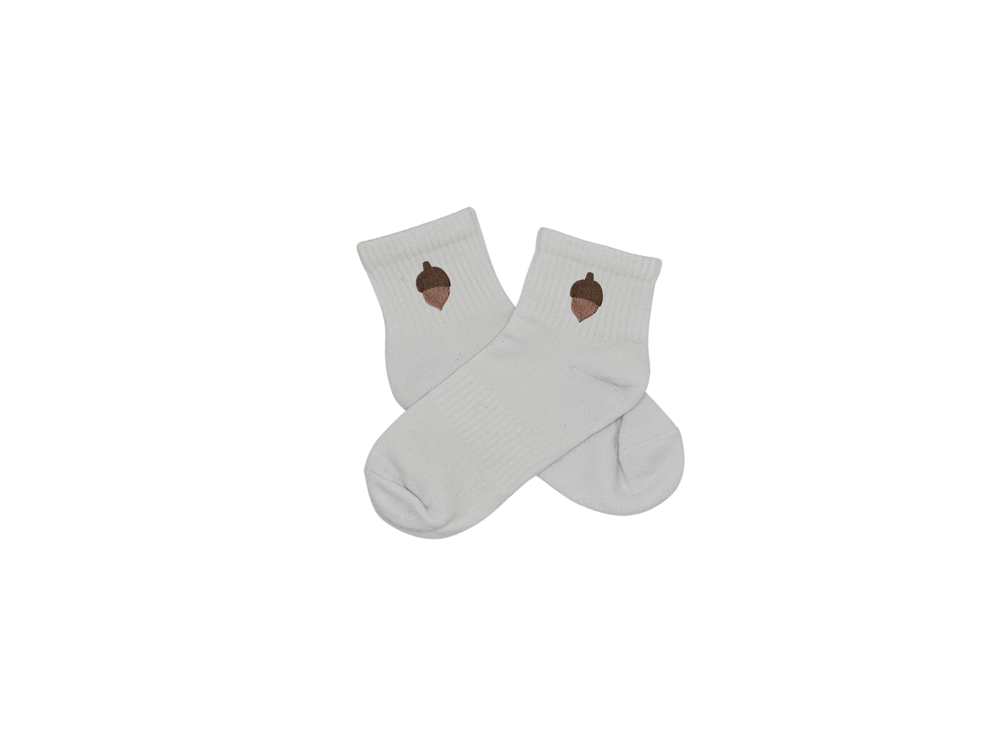 Chaussettes blanches courtes, 100% coton. Personnalisation des chaussettes grâce à des broderies. Il faut choisir parmi un choix de broderies dessinées à la main sur le thème de l’automne, saison automnale, Halloween, broderie cosy. La broderie est présente sur le côté extérieur des chaussettes. Toutes les broderies sont faites à la commande selon la personnalisation choisie. Ici, il s’agit de la broderie gland, marron.