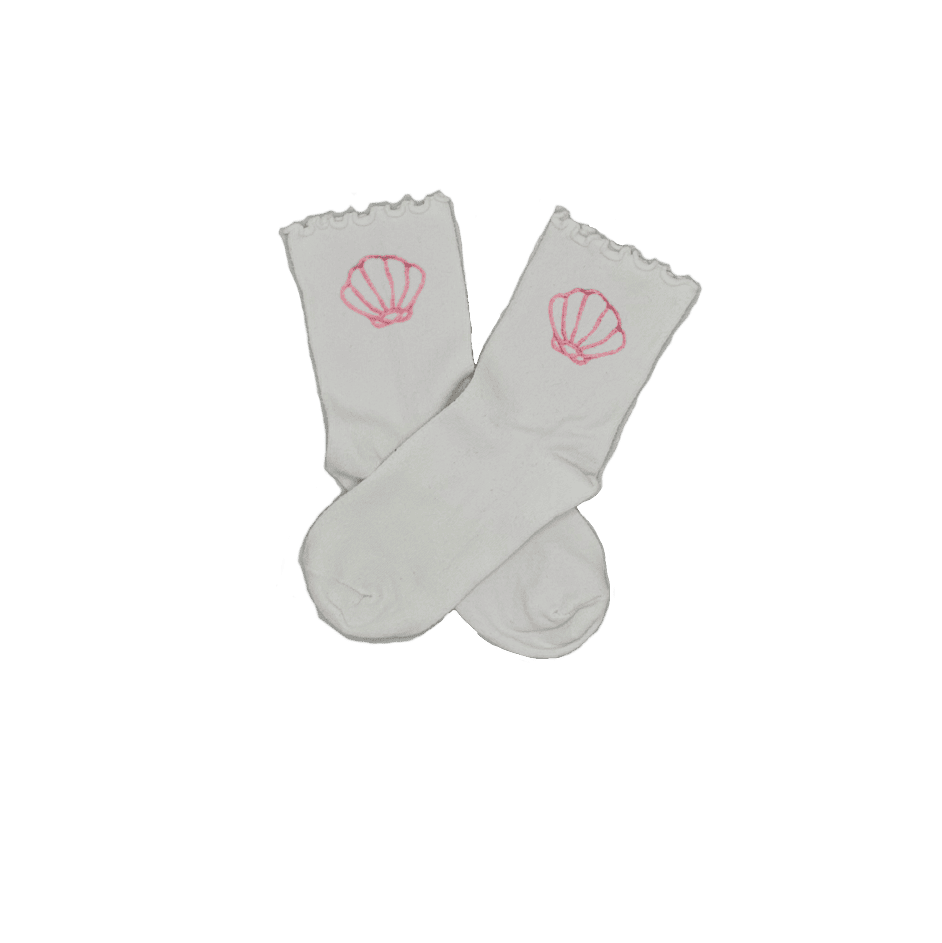 Chaussettes blanches courtes avec petits froufrous à l’extrémité, 100% coton. Personnalisation des chaussettes grâce à des broderies. Il faut choisir parmi un choix de broderies dessinées à la main sur le thème de l’été sur la Côte d’Azur dans les Alpes Maritimes, 06. La broderie est présente sur le côté extérieur des chaussettes. Toutes les broderies sont faites à la commande selon la personnalisation choisie. Ici, il s’agit de la broderie coquillage rose clair.