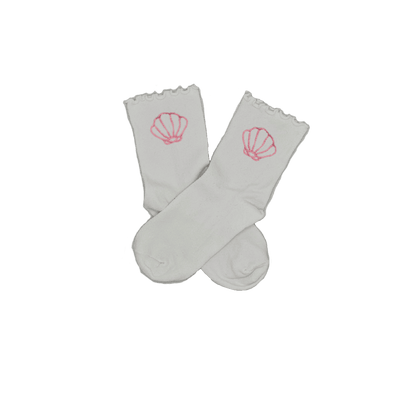 Chaussettes blanches courtes avec petits froufrous à l’extrémité, 100% coton. Personnalisation des chaussettes grâce à des broderies. Il faut choisir parmi un choix de broderies dessinées à la main sur le thème de l’été sur la Côte d’Azur dans les Alpes Maritimes, 06. La broderie est présente sur le côté extérieur des chaussettes. Toutes les broderies sont faites à la commande selon la personnalisation choisie. Ici, il s’agit de la broderie coquillage rose clair.