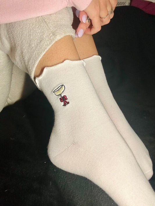Chaussettes blanches courtes avec petits froufrous à l’extrémité, 100% coton. Personnalisation des chaussettes grâce à des broderies. Il faut choisir parmi un choix de broderies dessinées à la main sur le thème de l’hiver, Noël, fêtes fin d’année, winter. La broderie est présente sur le côté extérieur des chaussettes. Toutes les broderies sont faites à la commande selon la personnalisation choisie. Ici, il s’agit de la broderie coupe de champagne avec un noeud rouge