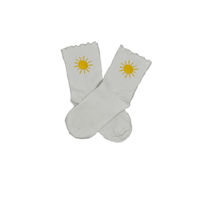 Chaussettes blanches courtes avec petits froufrous à l’extrémité, 100% coton. Personnalisation des chaussettes grâce à des broderies. Il faut choisir parmi un choix de broderies dessinées à la main sur le thème de l’été sur la Côte d’Azur dans les Alpes Maritimes, 06. La broderie est présente sur le côté extérieur des chaussettes. Toutes les broderies sont faites à la commande selon la personnalisation choisie. Ici, il s’agit de la broderie soleil jaune. 