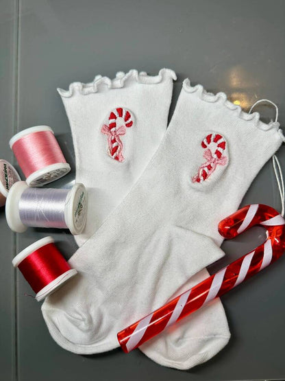 Chaussettes blanches courtes avec petits froufrous à l’extrémité, 100% coton. Personnalisation des chaussettes grâce à des broderies. Il faut choisir parmi un choix de broderies dessinées à la main sur le thème de l’hiver, Noël, fêtes fin d’année, winter. La broderie est présente sur le côté extérieur des chaussettes. Toutes les broderies sont faites à la commande selon la personnalisation choisie. Ici, il s’agit de la broderie sucre d'orge rouge, blanc, avec un noeud rose