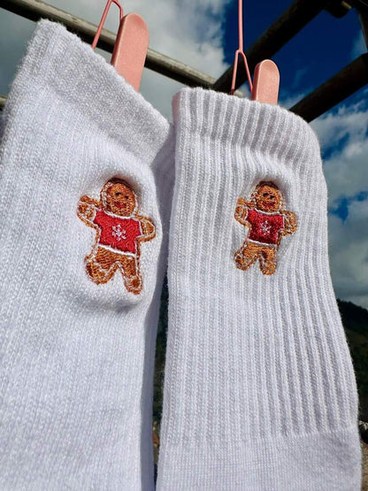 Chaussettes blanches hautes, 100% coton. Personnalisation des chaussettes grâce à des broderies. Il faut choisir parmi un choix de broderies dessinées à la main sur le thème de l’hiver, Noël, fêtes fin d’année, winter. La broderie est présente sur le côté extérieur des chaussettes. Toutes les broderies sont faites à la commande selon la personnalisation choisie. Ici, il s’agit de la broderie bonhomme en pain d'épices