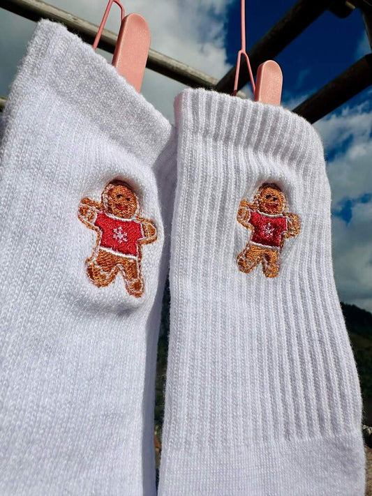 Chaussettes blanches hautes, 100% coton. Personnalisation des chaussettes grâce à des broderies. Il faut choisir parmi un choix de broderies dessinées à la main sur le thème de l’hiver, Noël, fêtes fin d’année, winter. La broderie est présente sur le côté extérieur des chaussettes. Toutes les broderies sont faites à la commande selon la personnalisation choisie. Ici, il s’agit de la broderie bonhomme en pain d'épices