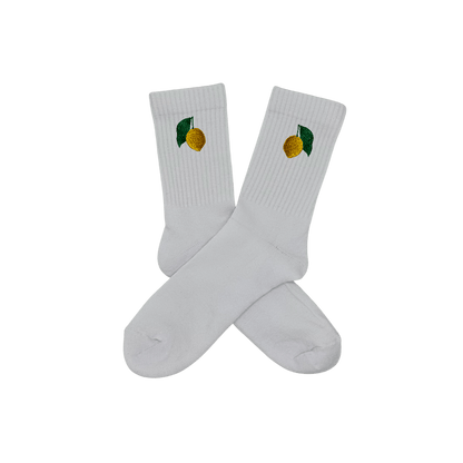 Chaussettes blanches hautes, 100% coton. Personnalisation des chaussettes grâce à des broderies. Il faut choisir parmi un choix de broderies dessinées à la main sur le thème de l’été sur la Côte d’Azur dans les Alpes Maritimes, 06. La broderie est présente sur le côté extérieur des chaussettes. Toutes les broderies sont faites à la commande selon la personnalisation choisie. Ici, il s’agit de la broderie citron de Menton, jaune et vert foncé. Emblème de la ville de Menton.