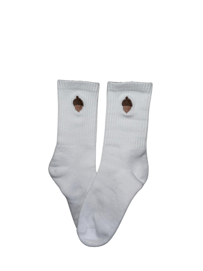 Chaussettes blanches hautes, 100% coton. Personnalisation des chaussettes grâce à des broderies. Il faut choisir parmi un choix de broderies dessinées à la main sur le thème de l’automne, saison automnale, Halloween, broderie cosy. La broderie est présente sur le côté extérieur des chaussettes. Toutes les broderies sont faites à la commande selon la personnalisation choisie. Ici, il s’agit de la broderie gland, marron.