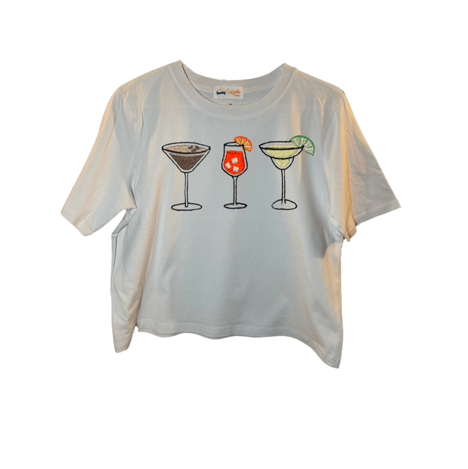 Crop top blanc, manche courte, large, 100% coton. Personnalisation du débardeur grâce à des broderies. Il faut choisir parmi un choix de broderies dessinées à la main sur le thème de l’été sur la Côte d’Azur dans les Alpes Maritimes, 06. Il faut aussi choisir la position de la broderie entre à gauche côté cœur, à droite ou au milieu. Toutes les broderies sont faites à la commande selon la personnalisation choisie. Ici, il s’agit de la broderie 3 cocktails : espresso martini, Aperol spritz et margarita. 