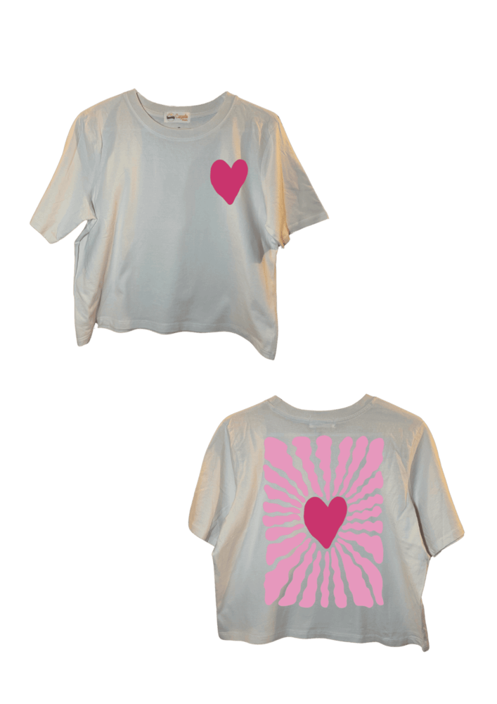 Crop top blanc court, manche courte, 100% coton. Personnalisation du crop top grâce à une technique de flocage, le DTF, pour une meilleure qualité d’impression et de tenue. La personnalisation est floquée à l’avant au niveau du cœur, en haut à gauche et à l’arrière en grand dans le dos. Ici, il s’agit de la personnalisation de DTF cœur rose. 