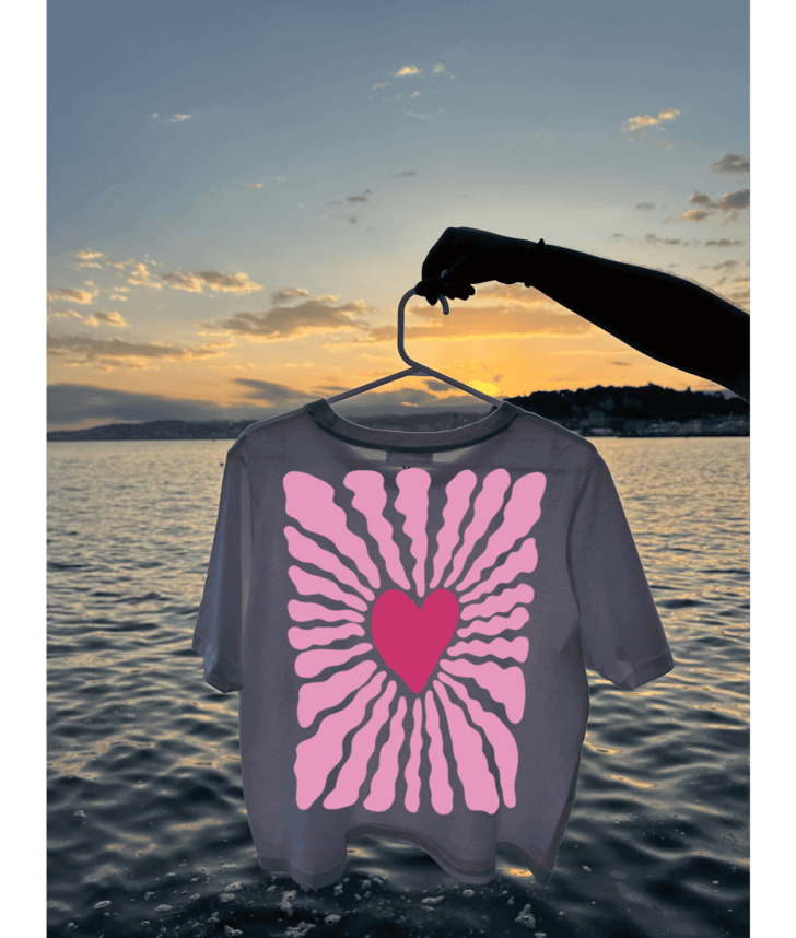 Crop top blanc de dos avec un coeur rose au centre et des traits en rose autour. Au dessus de l'eau, plage, mer, coucher de soleil