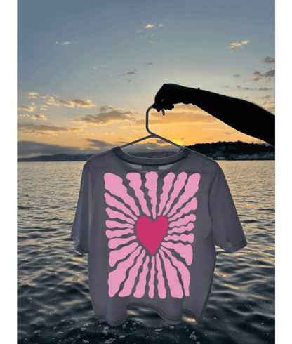 Crop top blanc de dos avec un coeur rose au centre et des traits en rose autour. Au dessus de l'eau, plage, mer, coucher de soleil