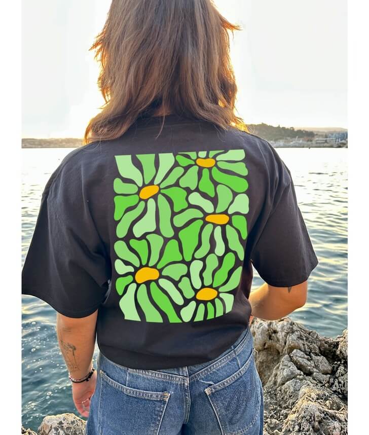 Modèle femme de dos portant un crop top noir en coton personnalisation flocage DTF en grand dans le dos fleur verte. Décor plage, mer, été, coucher de soleil.