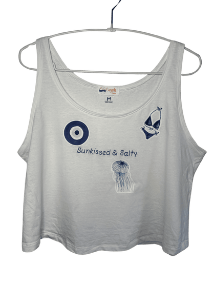 Débardeur blanc court, crop top, 100% coton. Personnalisation du débardeur grâce à des broderies et du flocage DTF. Toutes les broderies sont faites à la commande. Ici, il s’agit de la broderie écriture "sunkissed & salty". et flocage DTF bleu de l'oeil de sainte lucie d'un maillot de bain femme bleu et d'une méduse bleue.