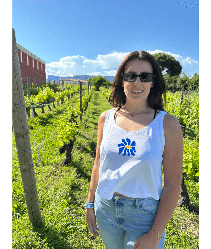 Modèle femme portant un débardeur blanc court en coton avec une personnalisation flocage DTF fleur bleue. Décor dans les vignes