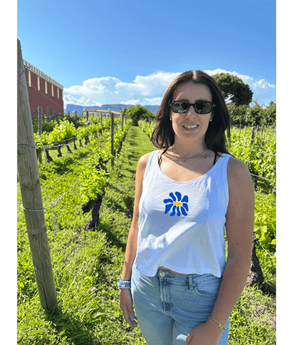 Modèle femme portant un débardeur blanc court en coton avec une personnalisation flocage DTF fleur bleue. Décor dans les vignes