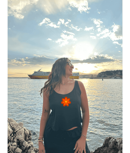 Débardeur noir court, crop top, 100% coton. Personnalisation du débardeur grâce à une technique de flocage, le DTF, pour une meilleure qualité d’impression et de tenue. La personnalisation est floquée au centre, en haut milieu. Ici, il s’agit de la personnalisation de DTF fleur orange seventies 70 milieu. Plage soleil été bord de l'eau mer coucher de soleil