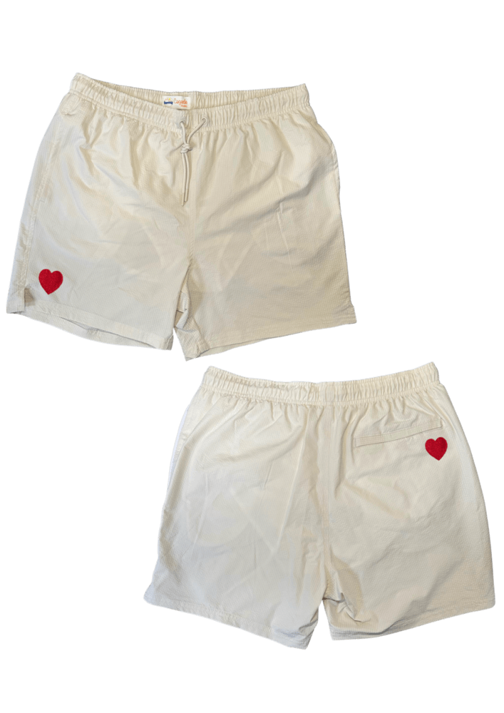 Maillot de plage pour homme couleur beige. Personnalisation du maillot grâce à des broderies. Il faut choisir parmi un choix de broderies dessinées à la main sur le thème de l’été sur la Côte d’Azur dans les Alpes Maritimes, 06. La broderie est brodée sur l’avant du maillot, jambe droite et sur la poche arrière jambe droite. Toutes les broderies sont faites à la commande selon la personnalisation choisie. Ici, il s’agit de la broderie coeur rouge