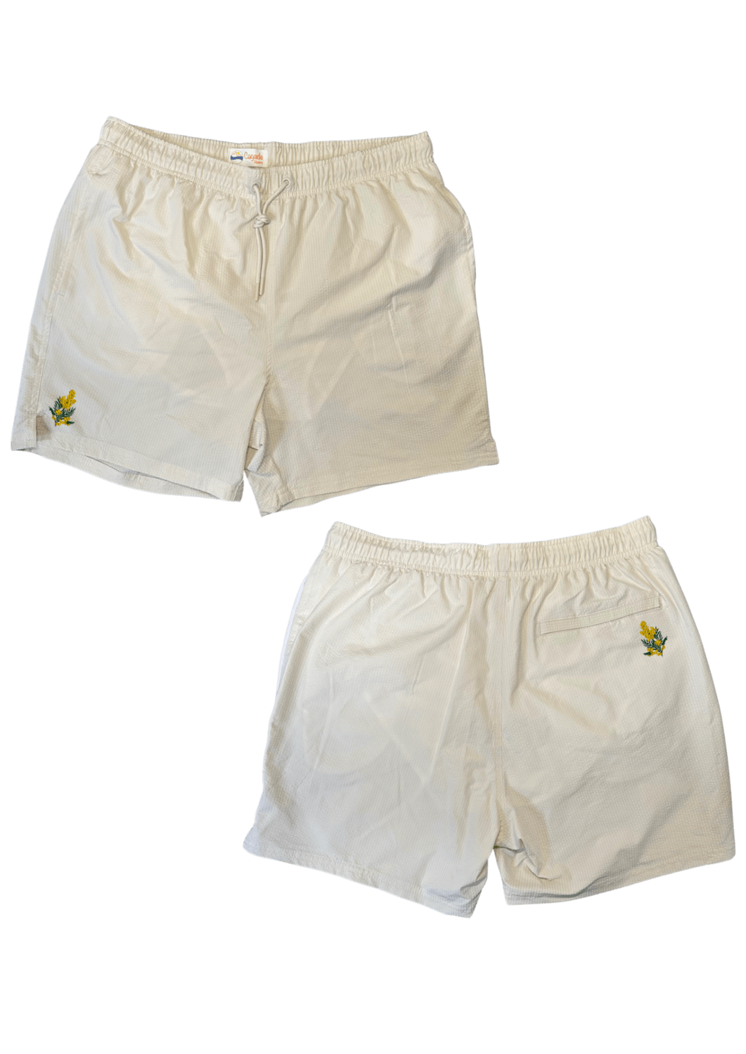 Maillot de plage pour homme couleur beige. Personnalisation du maillot grâce à des broderies. Il faut choisir parmi un choix de broderies dessinées à la main sur le thème de l’été sur la Côte d’Azur dans les Alpes Maritimes, 06. La broderie est brodée sur l’avant du maillot, jambe droite et sur la poche arrière jambe droite. Toutes les broderies sont faites à la commande selon la personnalisation choisie. Ici, il s’agit de la broderie mimosa, jaune et vert.