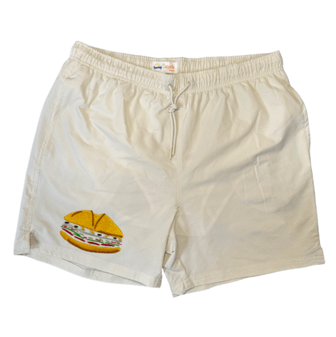 Maillot de plage pour homme couleur beige. Personnalisation du maillot grâce à des broderies. Il faut choisir parmi un choix de broderies dessinées à la main sur le thème de l’été sur la Côte d’Azur dans les Alpes Maritimes, 06. La broderie est brodée sur l’avant du maillot, jambe droite. Toutes les broderies sont faites à la commande selon la personnalisation choisie. Ici, il s’agit de la broderie pan bagnat. Sandwich emblématique de Nice, côte d'azur, 06.