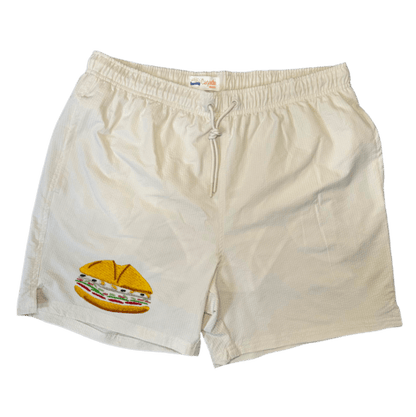 Maillot de plage pour homme couleur beige. Personnalisation du maillot grâce à des broderies. Il faut choisir parmi un choix de broderies dessinées à la main sur le thème de l’été sur la Côte d’Azur dans les Alpes Maritimes, 06. La broderie est brodée sur l’avant du maillot, jambe droite. Toutes les broderies sont faites à la commande selon la personnalisation choisie. Ici, il s’agit de la broderie pan bagnat. Sandwich emblématique de Nice, côte d'azur, 06.