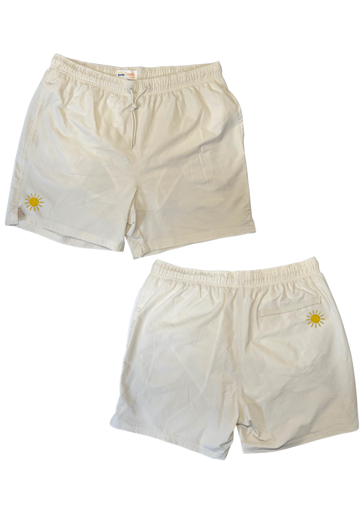 Maillot de plage pour homme couleur beige. Personnalisation du maillot grâce à des broderies. Il faut choisir parmi un choix de broderies dessinées à la main sur le thème de l’été sur la Côte d’Azur dans les Alpes Maritimes, 06. La broderie est brodée sur l’avant du maillot, jambe droite et sur la poche arrière jambe droite. Toutes les broderies sont faites à la commande selon la personnalisation choisie. Ici, il s’agit de la broderie soleil, jaune.