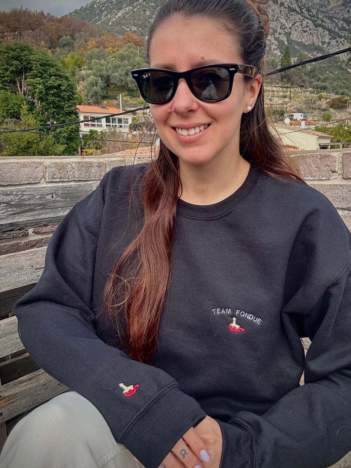 Sweatshirt noir tout doux hyper confortable loose avec broderie côté cœur et sur la manche droite personnalisation broderie team fondue. 
Texte TEAM FONDUE avec un appareil à fondue rouge et du fromage coulant idée cadeau à offrir personnalisation broderie. Broderie côté cœur plus broderie sur la manche droite. 