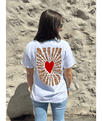 T-shirt oversize blanc, manche courte, 100% coton. Personnalisation du t-shirt grâce à une technique de flocage, le DTF, pour une meilleure qualité d’impression et de tenue. La personnalisation est floquée à l’avant au milieu en haut et à l’arrière en grand dans le dos. Ici, il s’agit de la personnalisation de DTF coeur léopard à l'avant et coeur rouge avec soleil léopard à l'arrière.
