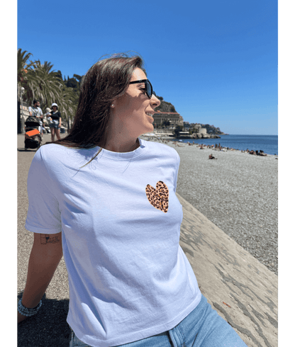 T-shirt oversize blanc, manche courte, 100% coton. Personnalisation du t-shirt grâce à une technique de flocage, le DTF, pour une meilleure qualité d’impression et de tenue. La personnalisation est floquée à l’avant au milieu en haut et à l’arrière en grand dans le dos. Ici, il s’agit de la personnalisation de DTF coeur léopard. Plage promenade des Anglais, Nice 06 été soleil.