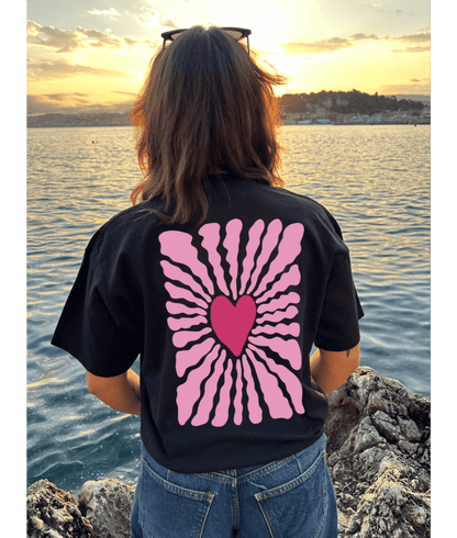 T-shirt oversize noir, manche courte, 100% coton. Personnalisation du t-shirt grâce à une technique de flocage, le DTF, pour une meilleure qualité d’impression et de tenue. La personnalisation est floquée à l’avant au milieu en haut et à l’arrière en grand dans le dos. Ici, il s’agit de la personnalisation de DTF coeur rose avant et arrière.