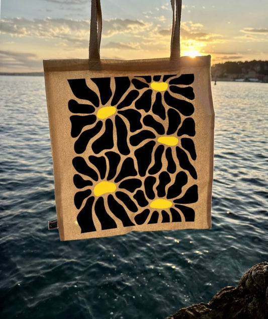 Tote bag, sac de course en coton. Personnalisation du débardeur grâce à une technique de flocage, le DTF, pour une meilleure qualité d’impression et de tenue. La personnalisation est floquée au centre, en haut milieu. Tout est fait à la commande selon la personnalisation choisie. Ici, il s’agit de la personnalisation de DTF, flocage fleur en noir. Décor mer, coucher de soleil.