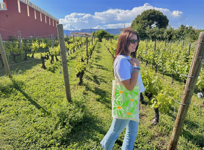 Tote bag, sac de course en coton. Personnalisation du débardeur grâce à une technique de flocage, le DTF, pour une meilleure qualité d’impression et de tenue. La personnalisation est floquée au centre, en haut milieu. Tout est fait à la commande selon la personnalisation choisie. Ici, il s’agit de la personnalisation de DTF, flocage fleur vert. Décor dans les vignes, femme avec le sac sur l'épaule, ciel bleu, château. 