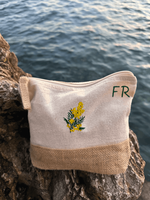 Trousse beige, écru, coton. Personnalisation de la trousse grâce à des broderies et initiales. Il faut choisir parmi un choix de broderies dessinées à la main sur le thème de l’été sur la Côte d’Azur dans les Alpes Maritimes, 06. Initiales brodées sur la trousse en haut à droite. Choix couleur du fil pour les initiales, personnalisation unique. Toutes les broderies sont faites à la commande selon la personnalisation choisie. Ici, il s’agit de la broderie mimosa, jaune et vert.
