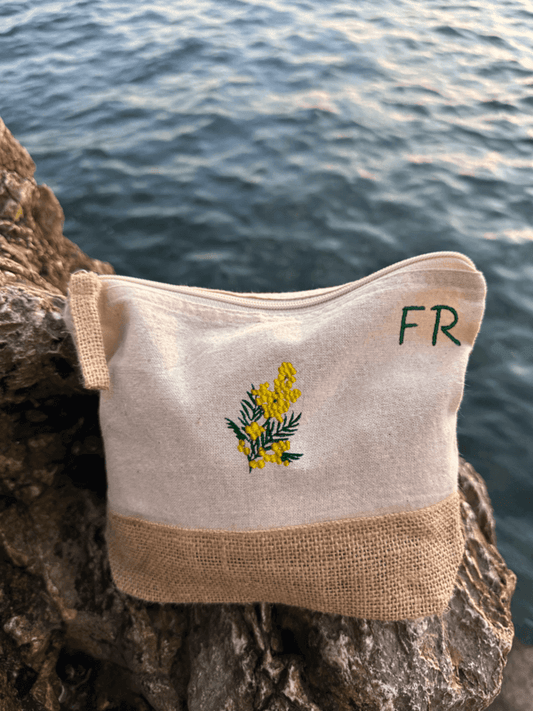 Trousse beige, écru, coton. Personnalisation de la trousse grâce à des broderies et initiales. Il faut choisir parmi un choix de broderies dessinées à la main sur le thème de l’été sur la Côte d’Azur dans les Alpes Maritimes, 06. Initiales brodées sur la trousse en haut à droite. Choix couleur du fil pour les initiales, personnalisation unique. Toutes les broderies sont faites à la commande selon la personnalisation choisie. Ici, il s’agit de la broderie mimosa, jaune et vert.
